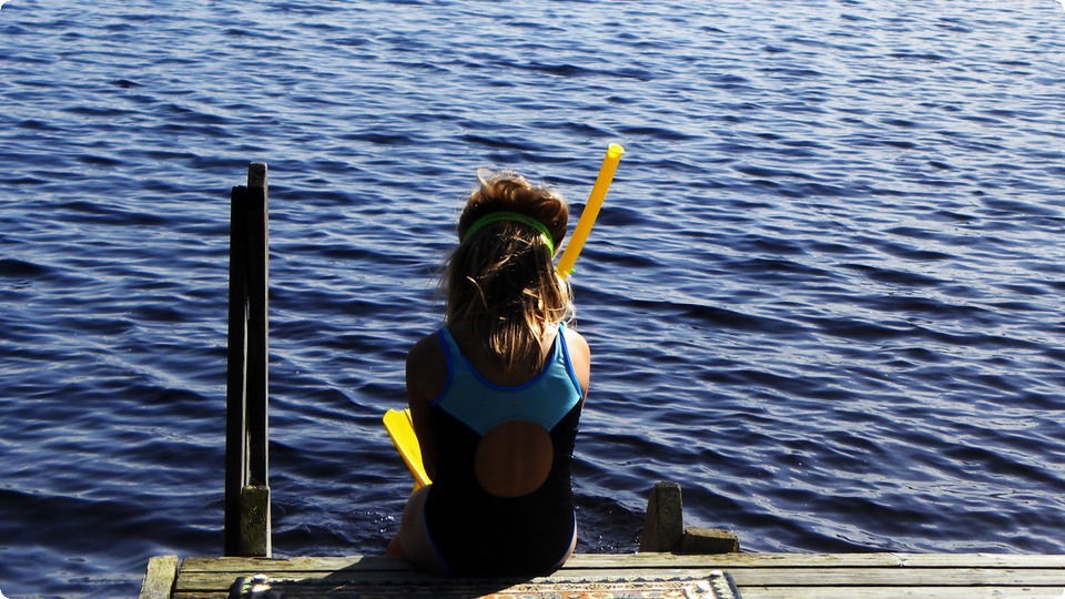 Flicka med snorkel sitter på kanten av brygga.