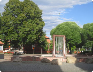 Bild från Mora centrum med fontän och grönskande träd.