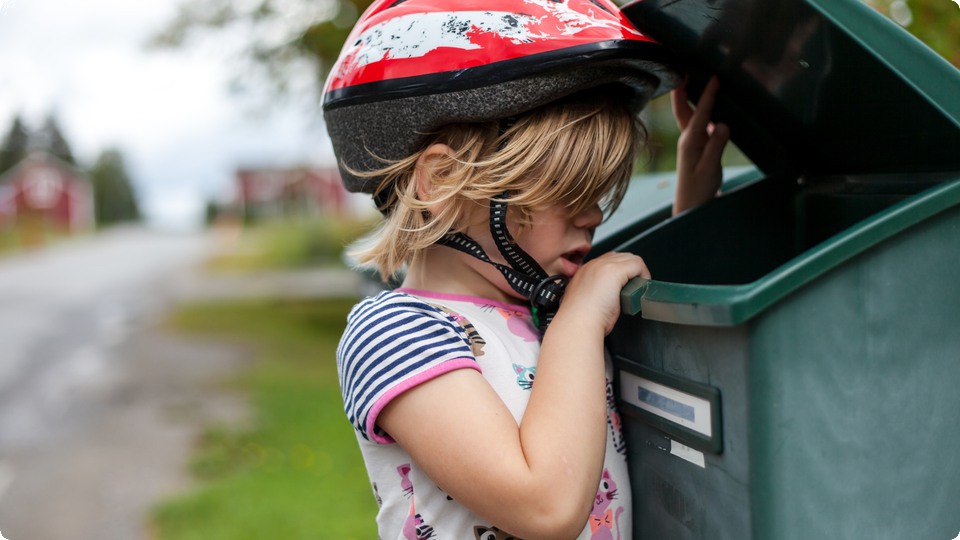 Barn med cykelhjälm på öppnar och tittar ner i brevlåda.