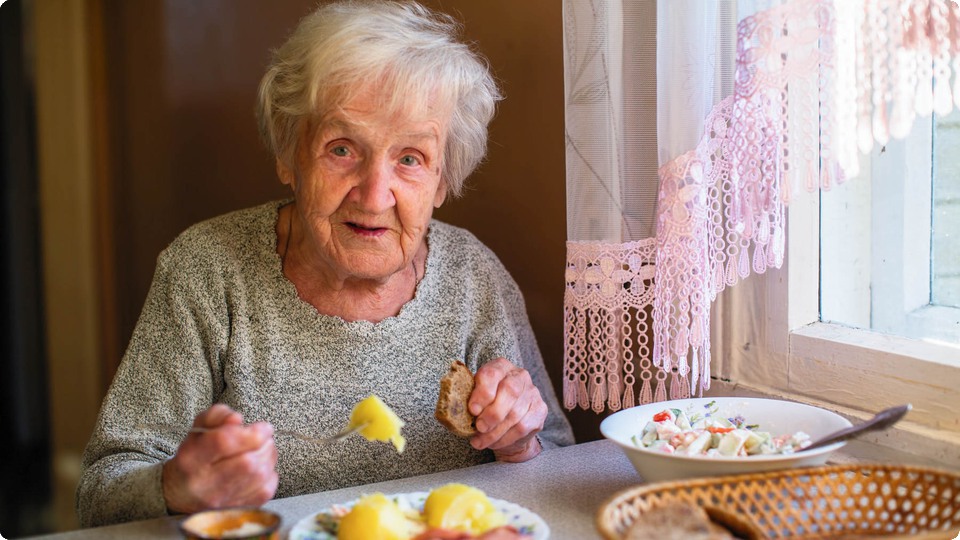 Pensionär äter mat vid sitt köksbord.