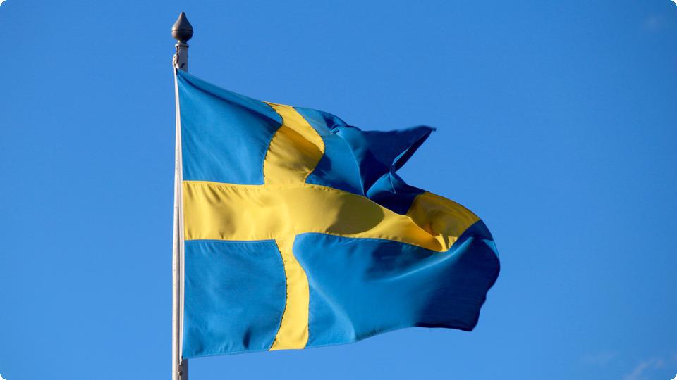 Foto av vajande svensk flagga mot blå himmel.