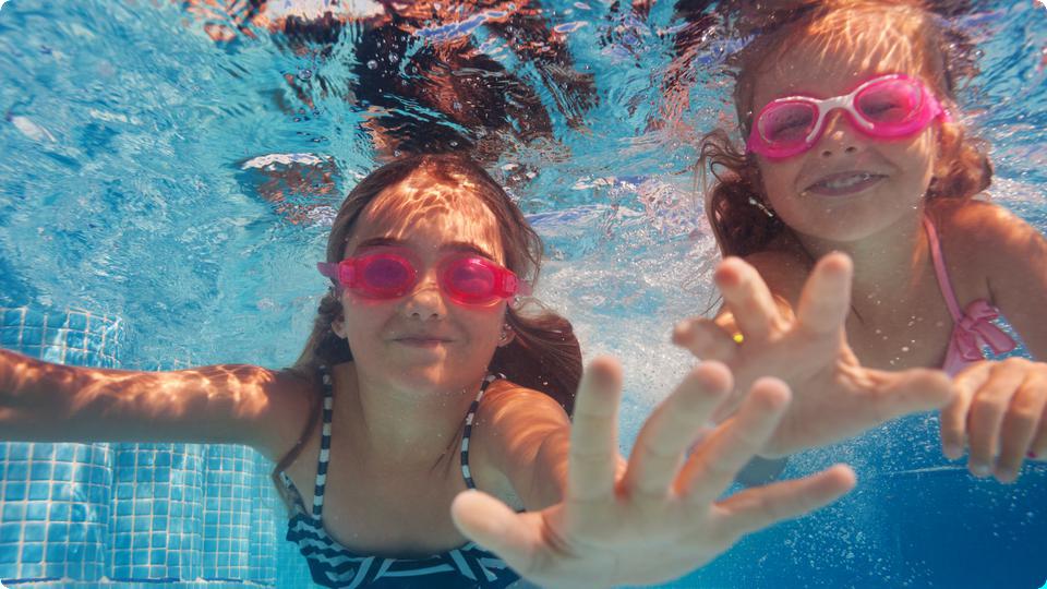 Undervattensbild på två glada tjejer med simglasögon.