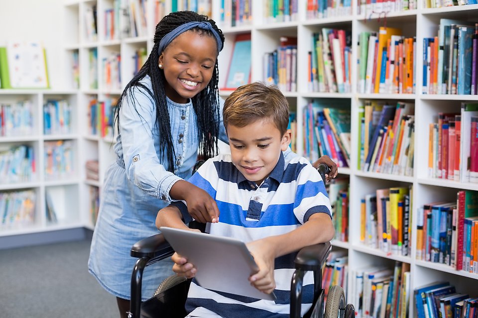 En flicka och en pojke på ett bibliotek tittar på en läsplatta.