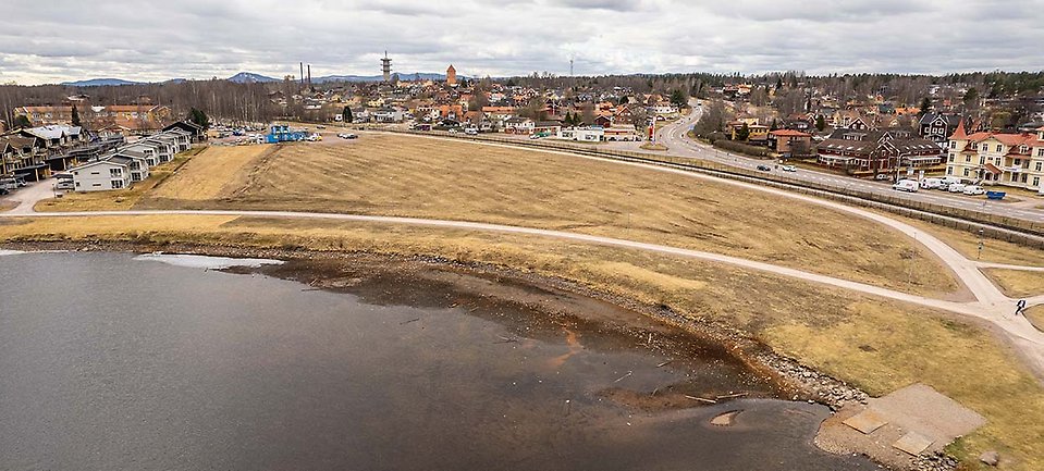 Flygbild över gräsområde vid vattenkanten i stadsmiljö.