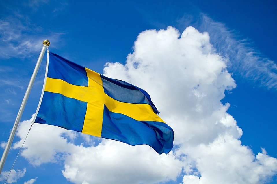 Svensk flagga mot molnig himmel.