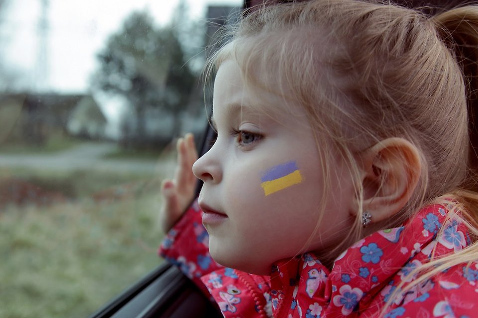 Flicka med ukrainska flaggan målad på kinden som tittar ut genom ett bilfönster.